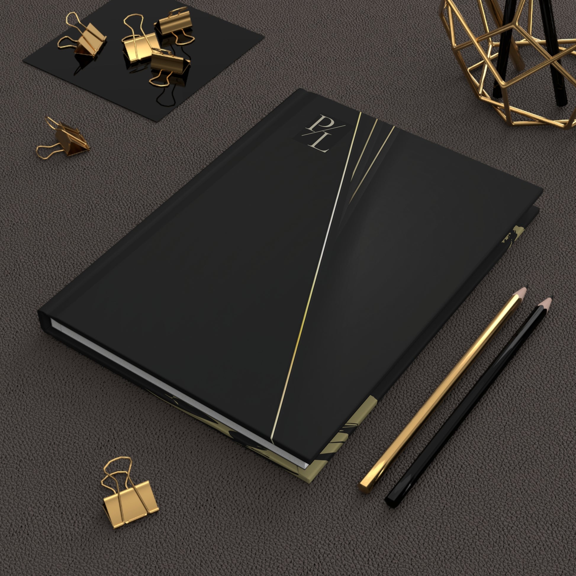 Black notebook with gold accents on a dark surface with office supplies.
